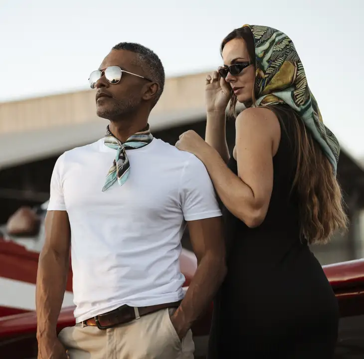 Couple portant des carrés de soie Maison Devienne près d’un avion, incarnant l’élégance, la liberté et l’inspiration polynésienne d’une création française de luxe.