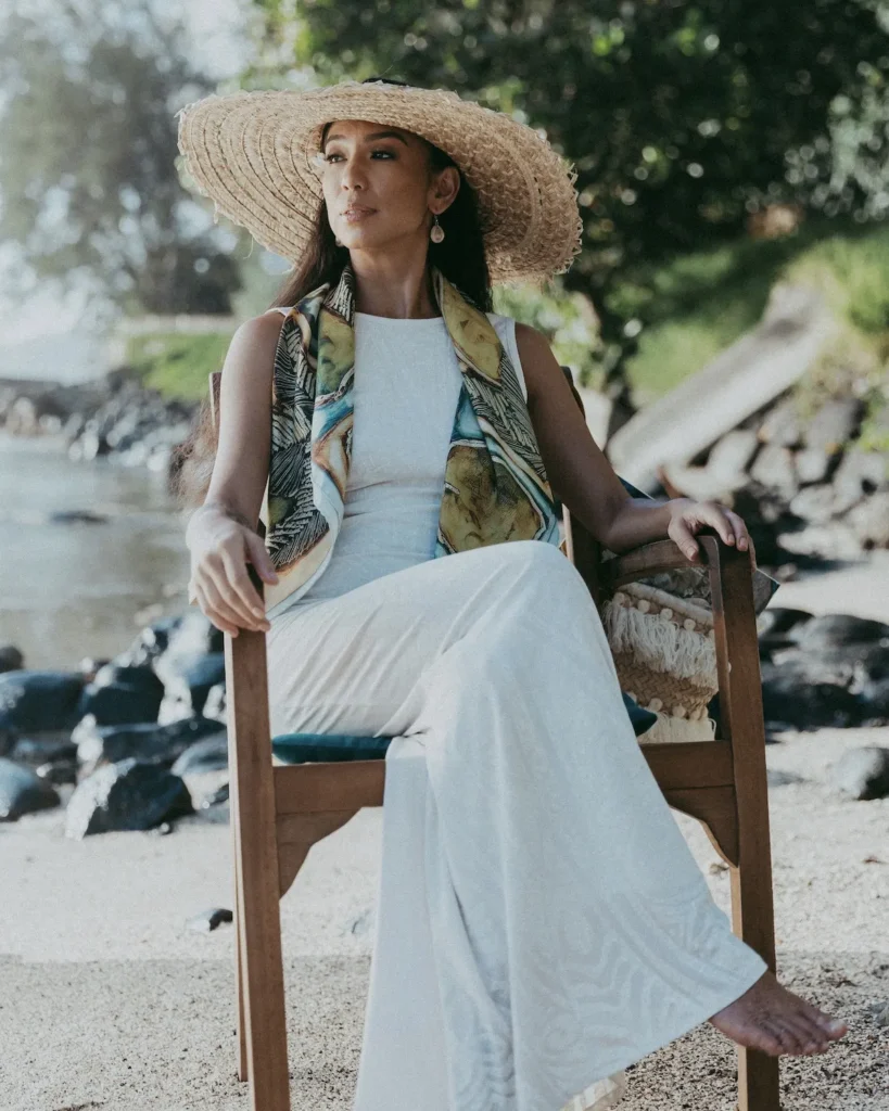 Femme assise en bord de mer à Tahiti portant un carré de soie Maison Devienne, symbole d’élégance naturelle et de savoir-faire français inspiré par la Polynésie.