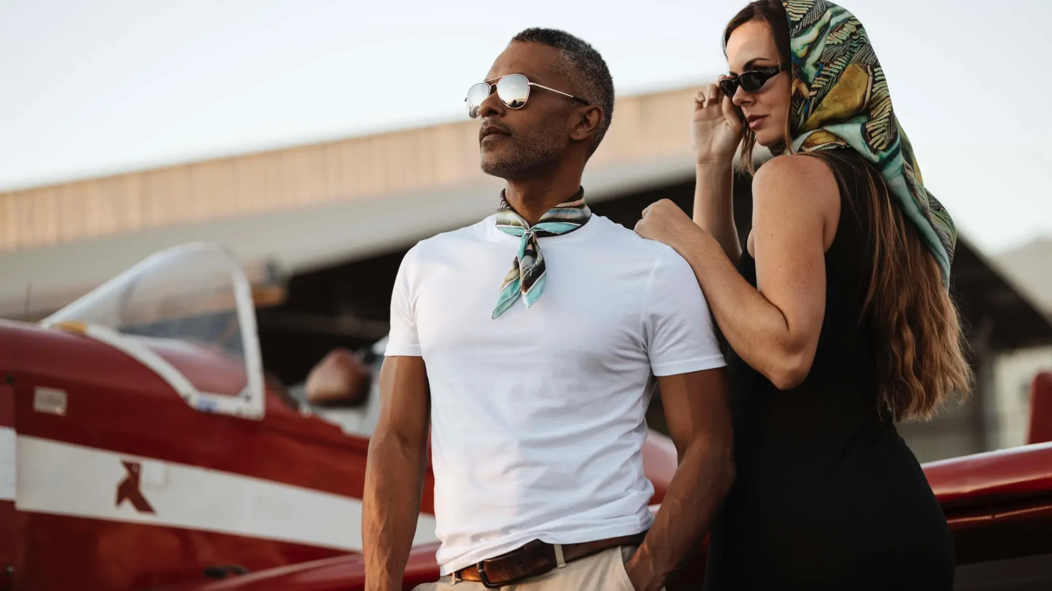 Couple portant des carrés de soie Maison Devienne près d’un avion, incarnant l’élégance, la liberté et l’inspiration polynésienne d’une création française de luxe.