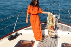 Femme en robe orange avec un carré de soie Maison Devienne sur un bateau
