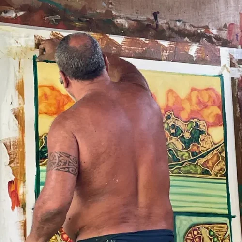 Louis, artiste de Maison Devienne, peignant à la main les motifs polynésiens qui inspirent les carrés de soie, symbole d’un savoir-faire artistique unique à Tahiti.